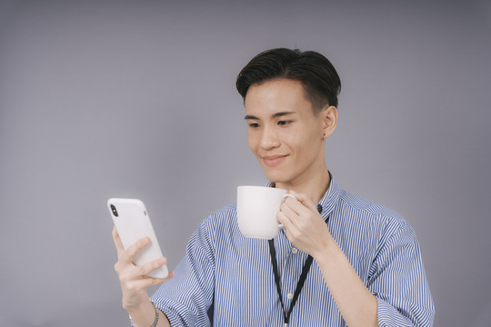 穿着蓝领衬衫的泰国帅哥用智能手机喝咖啡。