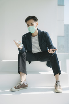 时尚写真-年轻的泰国亚裔男子在家隔离自己。戴着医生面罩拿着酒精凝胶。