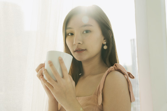 美丽的亚泰女人早上在房间里拿着白色的咖啡杯。