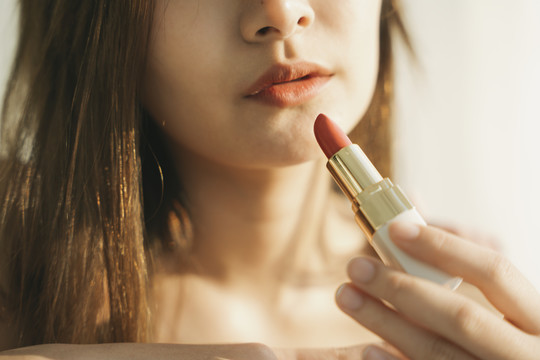 靠近美丽的亚洲泰国女人手里拿着口红。化妆品概念。早晨温暖的灯光。