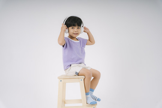 小买紫t恤坐在木椅上，用白色耳机欣赏音乐。