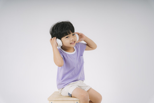 小买紫t恤坐在木椅上，用白色耳机欣赏音乐。