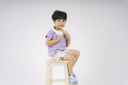 穿着紫色t恤的小男孩坐在木椅上，脖子上戴着白色耳机。