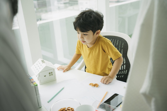 小男孩在客厅的桌子旁做作业，爸爸教他在上班前做功课。