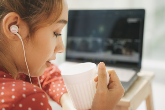 从家工作的概念-特写美丽的年轻女子穿着红色睡衣衬衫喝咖啡从一个杯子在笔记本电脑前。检疫。