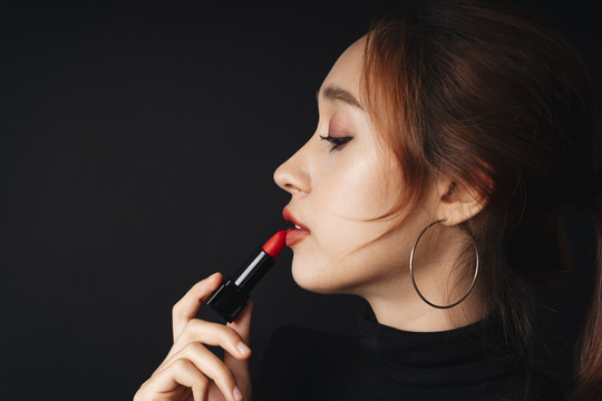 侧视图特写肖像美丽的年轻女子穿着黑色毛衣隔离黑暗的背景。女人用红色唇膏。化妆品概念。