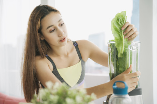 穿着运动内衣的健康年轻女子在厨房用榨汁机勾兑新鲜蔬菜汁，准备营养丰富的维生素包装饮料。健康饮食，素食