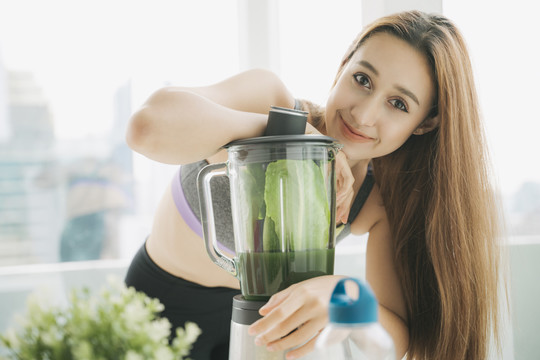 穿着运动内衣的健康年轻女子在厨房用榨汁机勾兑新鲜蔬菜汁，准备营养丰富的维生素包装饮料。健康饮食，素食