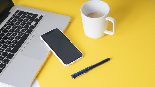 背景-现代办公室里黄色的商务人士工作桌和一杯咖啡、钢笔、智能手机、笔记本电脑。