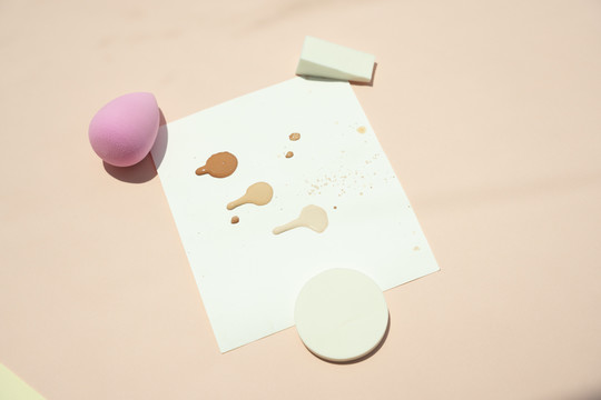 粉扑海绵和液体化妆品在米色背景的试纸上。