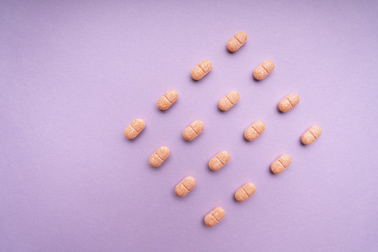 顶视图-紫粉色背景上的橙色药丸。方形。