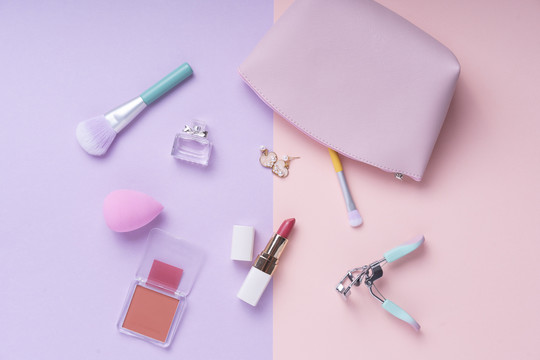 粉彩粉色和紫色桌子上的化妆品顶视图。工作场所和化妆包。