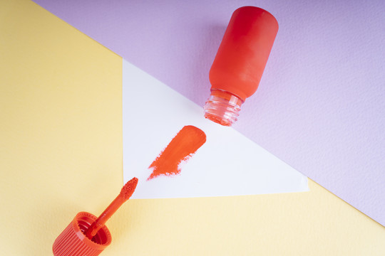 化妆唇刷和液体唇膏的红色瓶特写在彩色背景与版权空间。