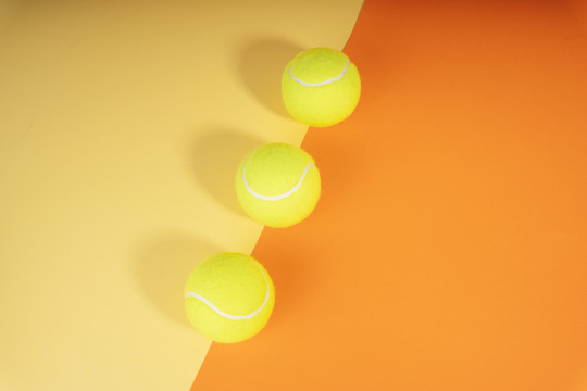 橙色和黄色球场上有三个网球。顶视图。平铺。