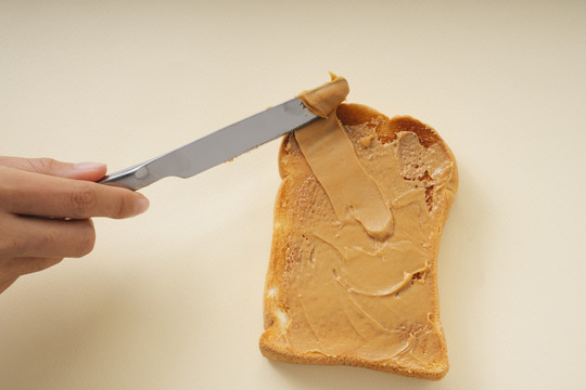 用刀把花生酱放在面包片上的人。