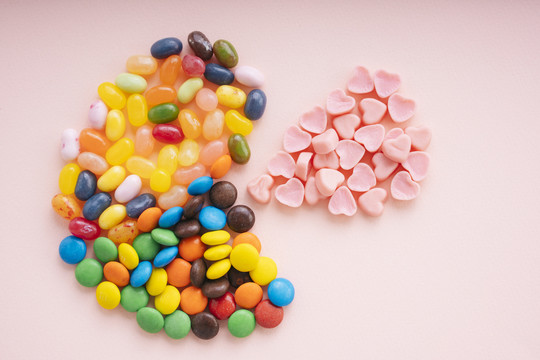 吃豆人概念。混合五颜六色糖果燕子心形糖果粉红色背景。