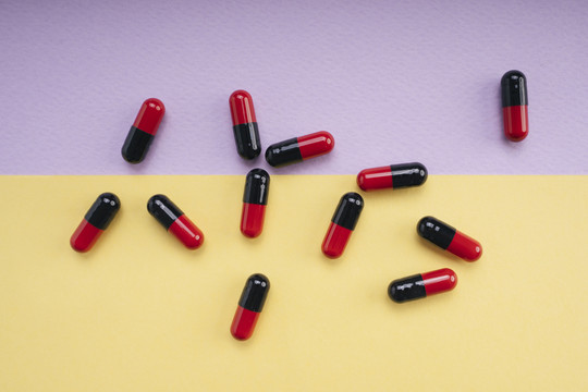 顶视图-粉彩背景上的黑色和红色药丸胶囊。