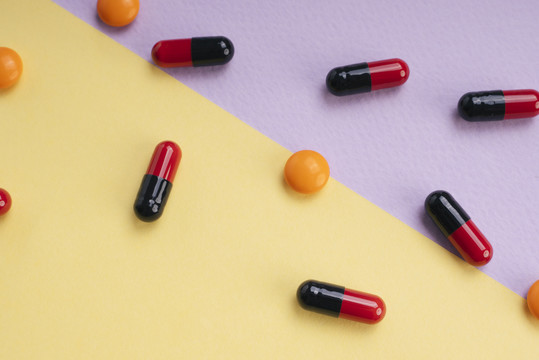 顶视图-红色和黑色药丸胶囊和橙色圆圈药丸在粉彩背景。