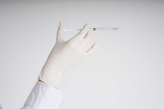 医生用塑料手套手持注射器隔离白色背景。