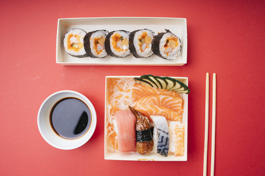 顶视图-红色背景上的日本寿司和生鱼片盒。