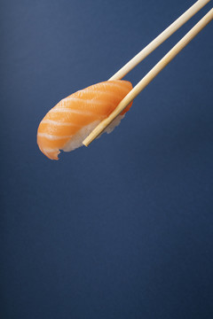 用筷子在蓝色背景上吃新鲜的三文鱼寿司。