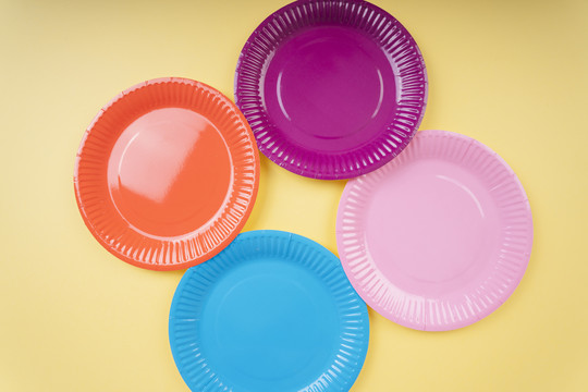 黄色米色背景上的四个彩色塑料盘子。橙色。紫色。蓝色。粉红色。