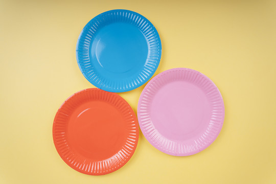 黄色米色背景上的四个彩色塑料盘子。橙色。蓝色。粉红色。