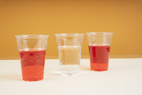 两个红色苏打水和淡水的塑料杯，一个在橙色背景上。