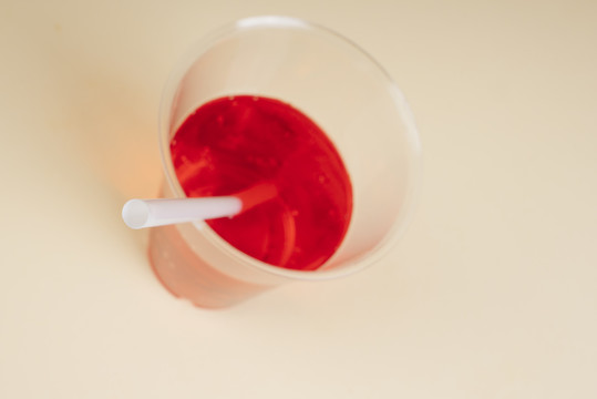 桌上放着吸管的塑料杯里的红色起泡水。闭合。