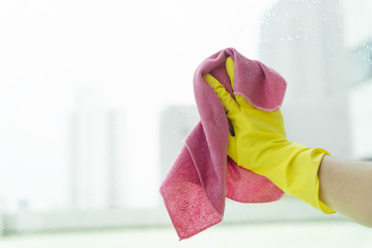 女佣手戴黄色手套，用粉色抹布擦镜子。Covid-19冠状病毒预防。