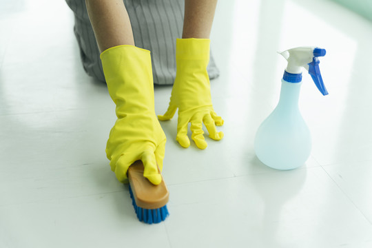 女佣戴手套用刷子和洗涤剂喷雾瓶清洁地板。
