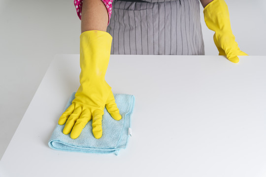 女佣戴手套用抹布擦餐桌。Covid-19冠状病毒预防。