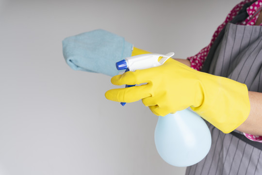 女佣戴着黄色防护手套，手里拿着抹布和洗涤剂喷雾瓶。
