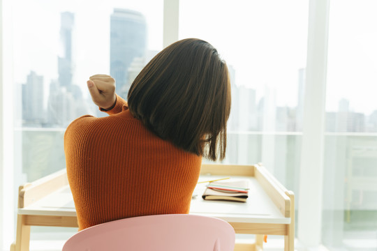 后视图-美丽的年轻亚泰黑人短发女子在橙色毛衣伸展手臂和身体后，研究从家里。