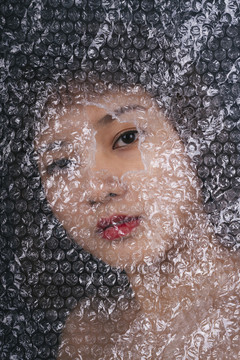 一名亚裔泰国妇女在塑料袋后面，眼睛盯着一个洞。特写肖像。