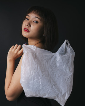 美丽的亚泰妇女短发塑料袋隔离黑色背景。特写肖像。塑料时尚。