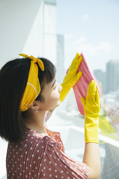 女服务员戴着黄色防护手套，用干抹布擦着公寓的玻璃窗。