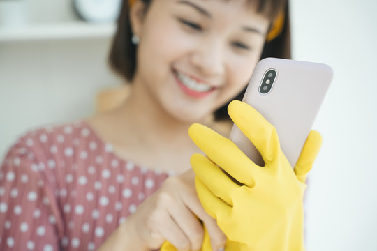特写-快乐美丽的女佣戴着黄色防护手套使用智能手机。女佣服务申请。