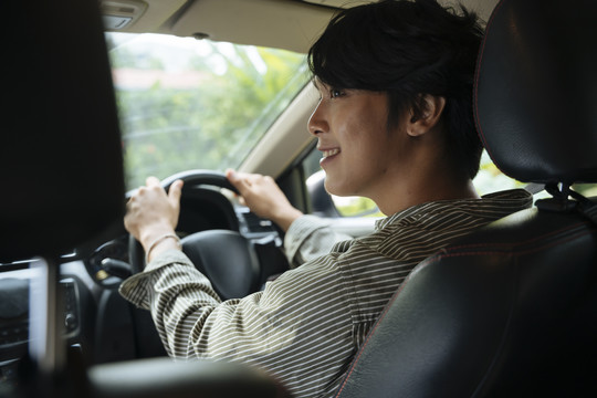 快乐的年轻帅气的亚泰男人微笑着在座位前开车。
