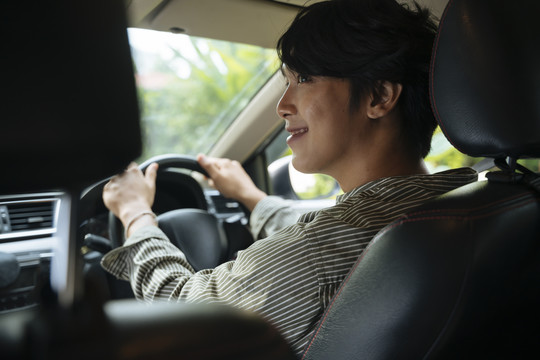快乐的年轻帅气的亚泰男人微笑着在座位前开车。