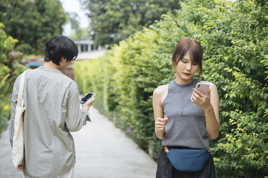 亚泰女子在公园慢跑，看着智能手机上的音乐播放列表，从男子身边走过。