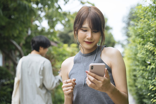 亚泰女子在公园慢跑，看着智能手机上的音乐播放列表，从男子身边走过。