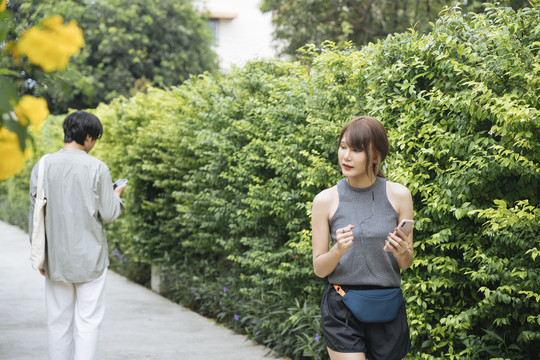 亚泰女子在公园慢跑，看着智能手机上的音乐播放列表，从男子身边走过。