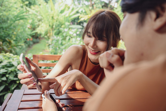 快乐美丽的亚泰女人和男朋友一起看智能手机屏幕。检查旅游目的地或有趣的餐厅咖啡厅。