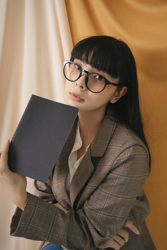 美丽的亚泰长黑发女子戴着眼镜带着一本黑色的书。女商人的时尚肖像。在hone工作。