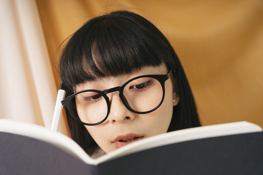特写-美丽的亚泰黑发女子戴眼镜看书。漂亮的书呆子女人在书上做笔记。
