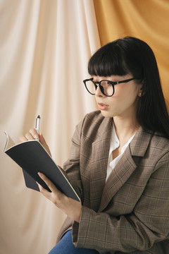 体贴美丽的亚泰长黑发女人穿着夹克套装拿着一本书和一支笔。时尚肖像。