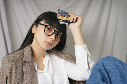 特写-美丽的亚泰黑发女子戴着眼镜拿着信用卡银行。时尚肖像。