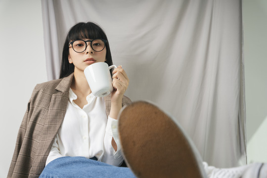 时尚写真——美丽的亚泰黑发长发白衬衫女人戴着眼镜端着一杯热咖啡。