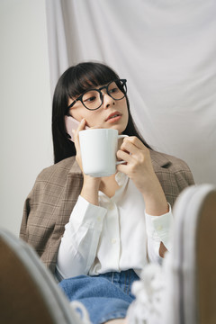 时尚写真-美丽的亚泰黑头发长白衬衫的女人戴着眼镜拿着一杯热咖啡和智能手机。